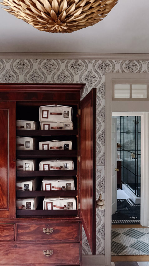 Handsome wooden cabinet filled with labeled fabric storage bins in a stylish, vintage-inspired home interior setting.