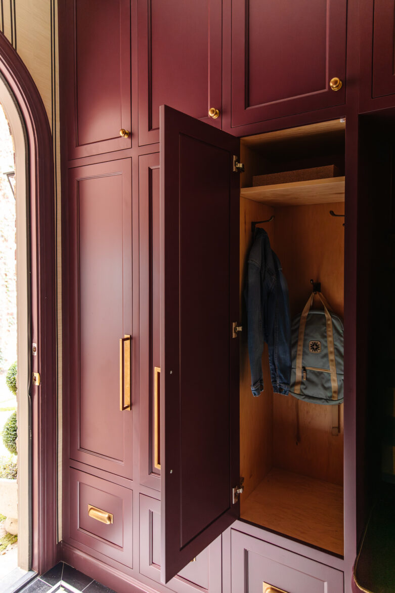 High-quality burgundy built-in closet with gold hardware, perfect for organized entryway or mudroom storage.