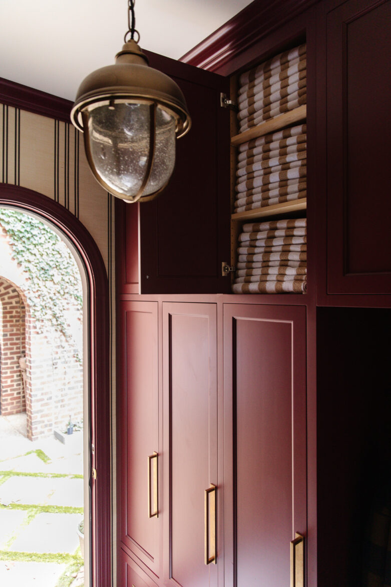 High-end burgundy cabinets with gold handles, featuring linen towels on open shelves. Elegant lighting and stylish design create a cozy, sophisticated space.
