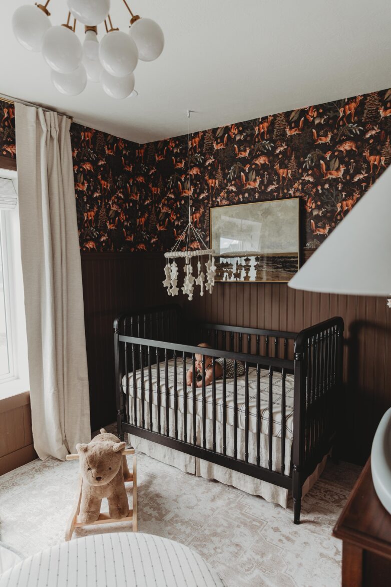Versatile baby crib set up in a stylish nursery with woodland wallpaper, plush teddy bear, modern lighting, and soft curtains.
