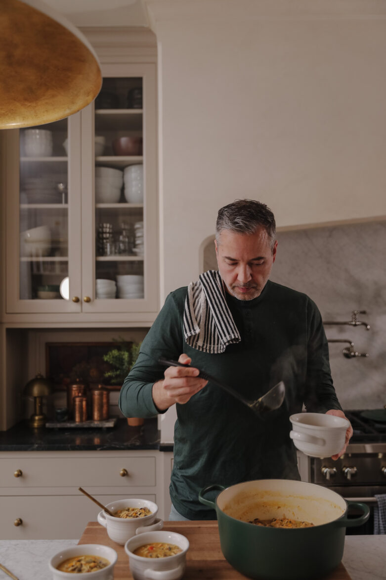 Chris cooking in a modern kitchen a large pot of soup on the stove, surrounded by bowls of ingredients, creating a warm and inviting atmosphere.