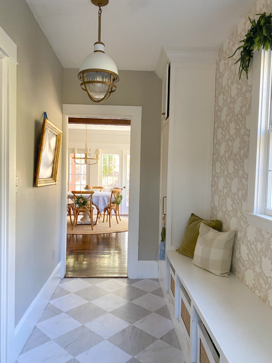 Bright entryway featuring stylish peel-and-stick floor tiles in a subtle diamond pattern. The space includes a built-in bench with cushions, a decorative wall, and a view into a dining area with natur.
