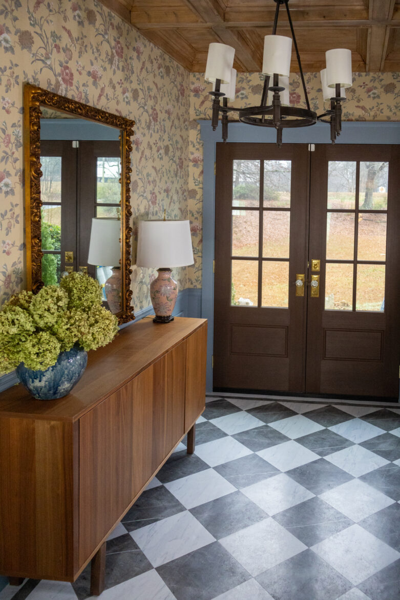 Bright entryway featuring stylish peel-and-stick floor tiles in a black and white checkerboard pattern. Elegant chandelier, floral wallpaper, and vintage mirror create a welcoming atmosphere.