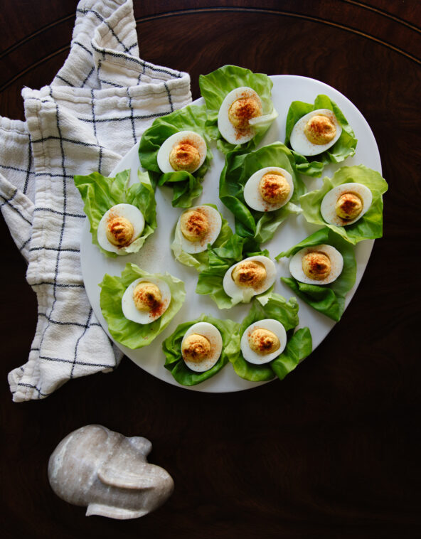 Delicious deviled eggs served on fresh green lettuce leaves, arranged on a white platter with a rustic cloth and stone heart, perfect for healthy appetizers and family gatherings.