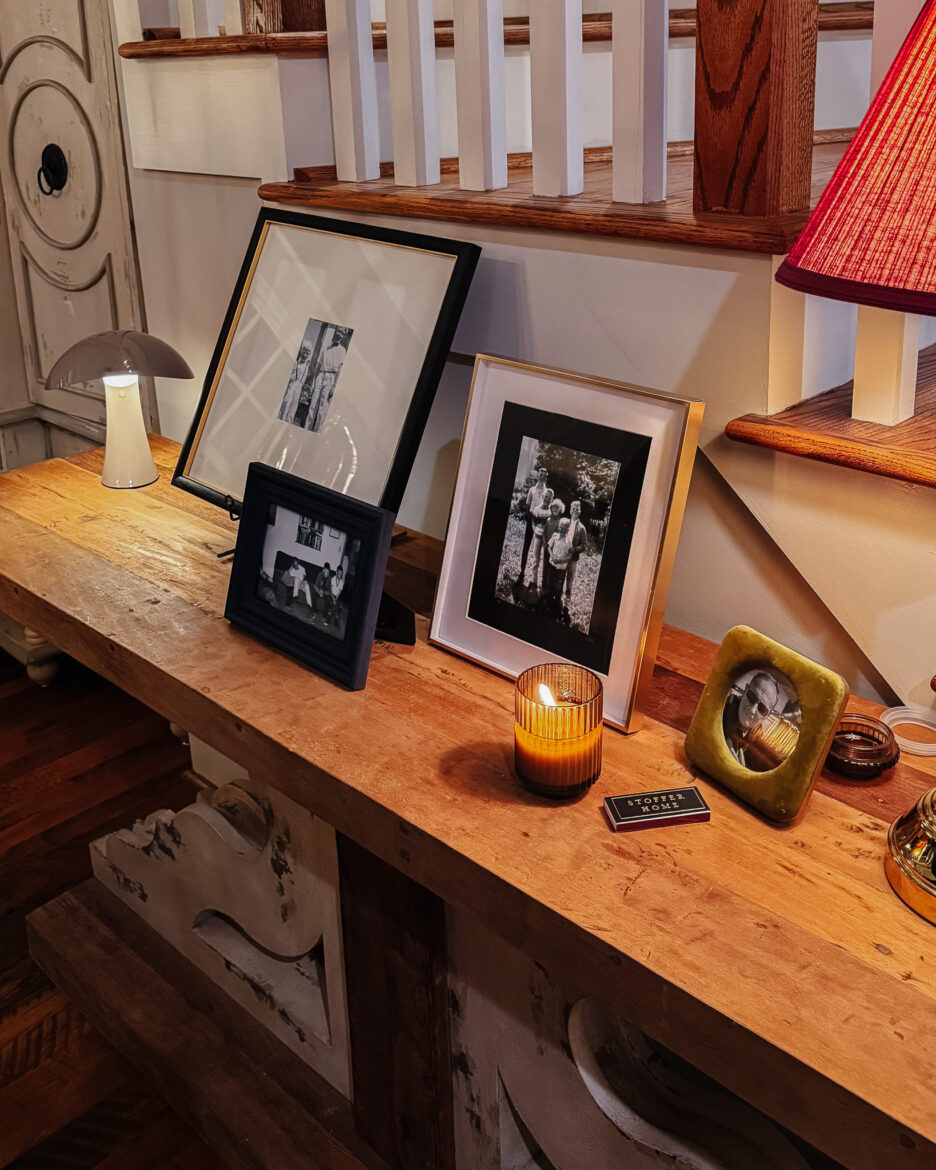A rustic wooden console table displaying framed black-and-white photos, a candle, and decorative items in a warm, inviting living space.