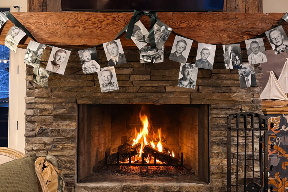 A warm fireplace decorated with a black-and-white family photos garland hanging above, creating a welcoming and nostalgic atmosphere in a home living room.