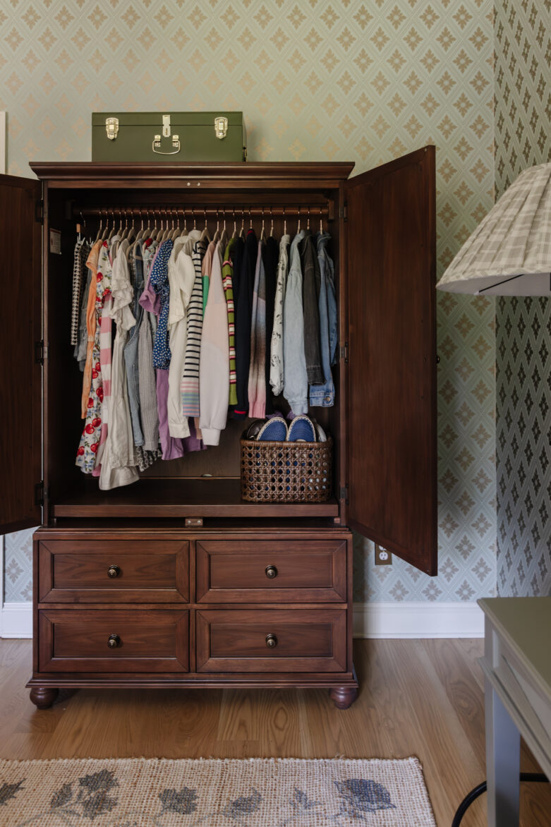 A dark traditional wardrobe with kids clothing and four drawers underneath