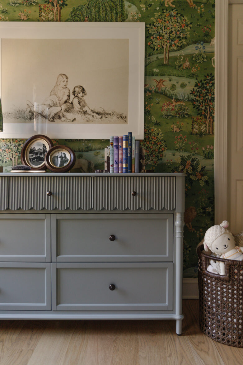 Elegant coastal blue dresser in a vintage-style room with decorative items, framed artwork, and a woven basket with plush toys, creating a cozy and stylish nursery or bedroom space.