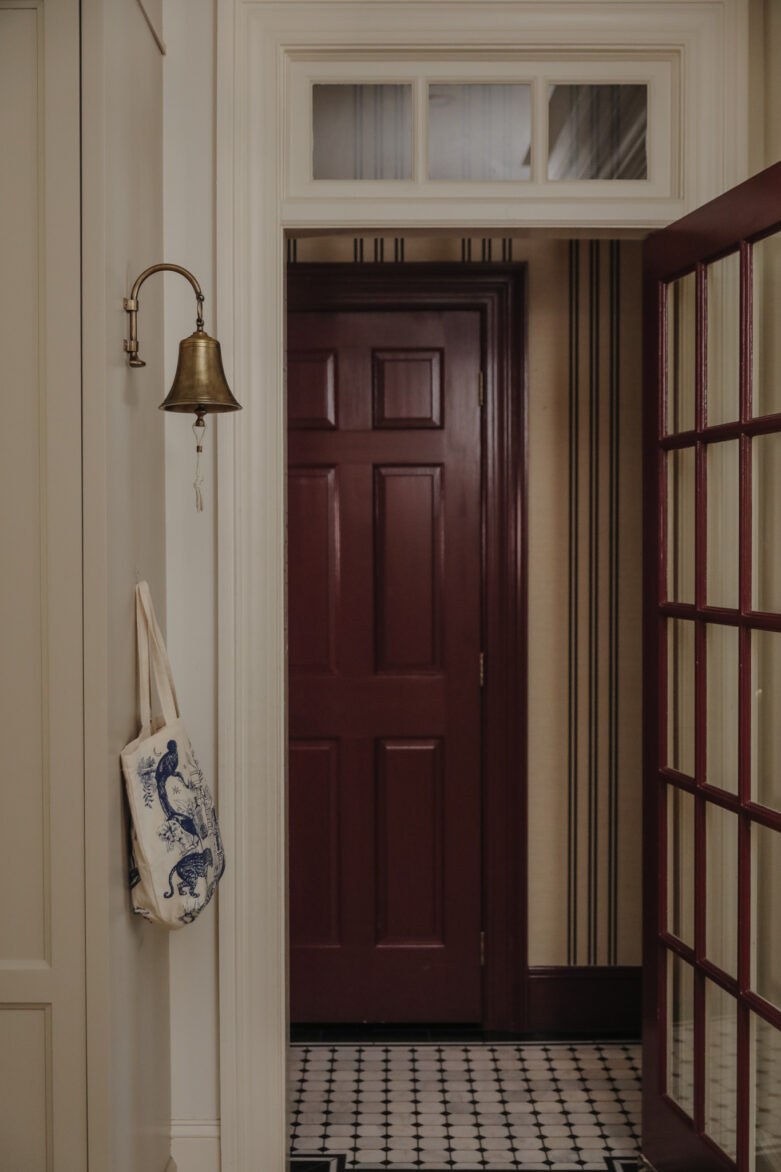 Inviting entryway featuring a rich burgundy door, vintage dinner bell, and patterned tile floor, creating a warm and welcoming atmosphere.