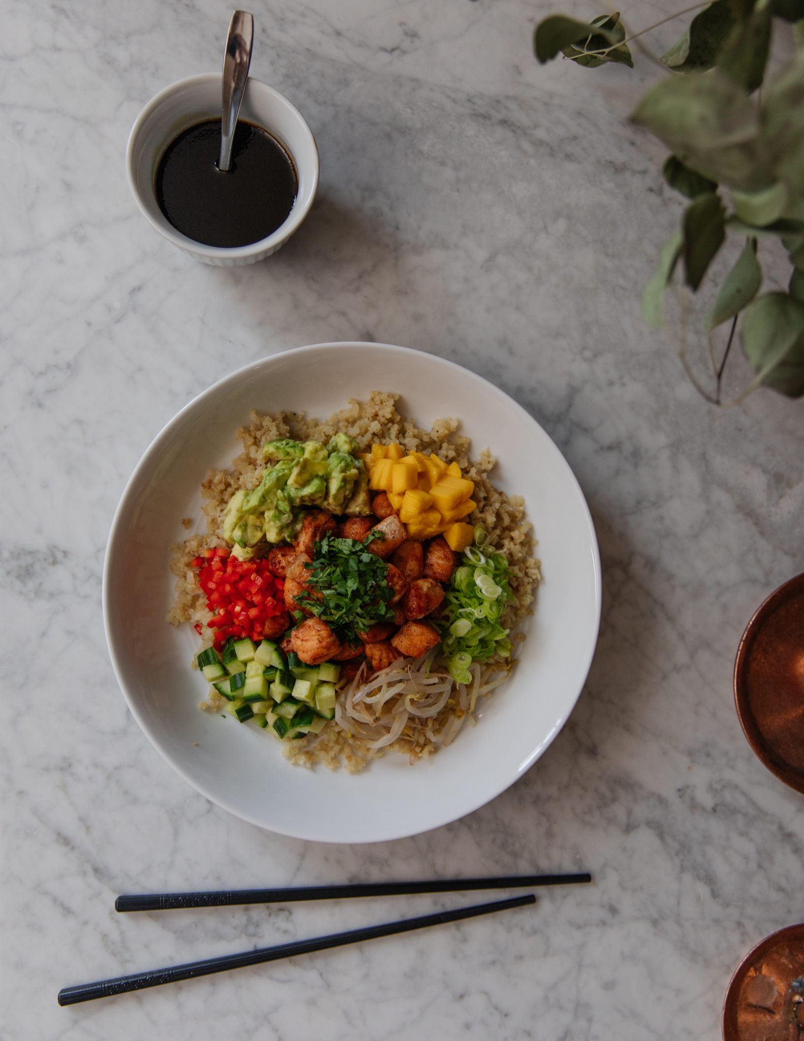 Healthy Asian rice bowl with vegetables, mango, cucumber, and salmon, garnished with green onions and served with Asian-style sauce.