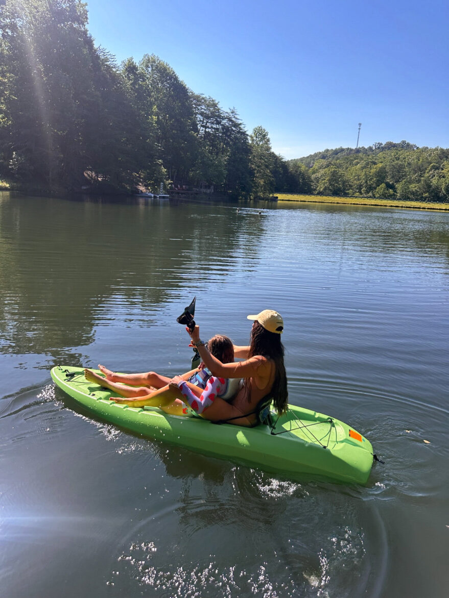 Woman and child kayaking on a peaceful lake surrounded by trees, enjoying a sunny day outdoors.