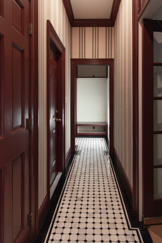 Long hallway with black & white marble tile pattern and a beige striped grasscloth wallpaper on the wall