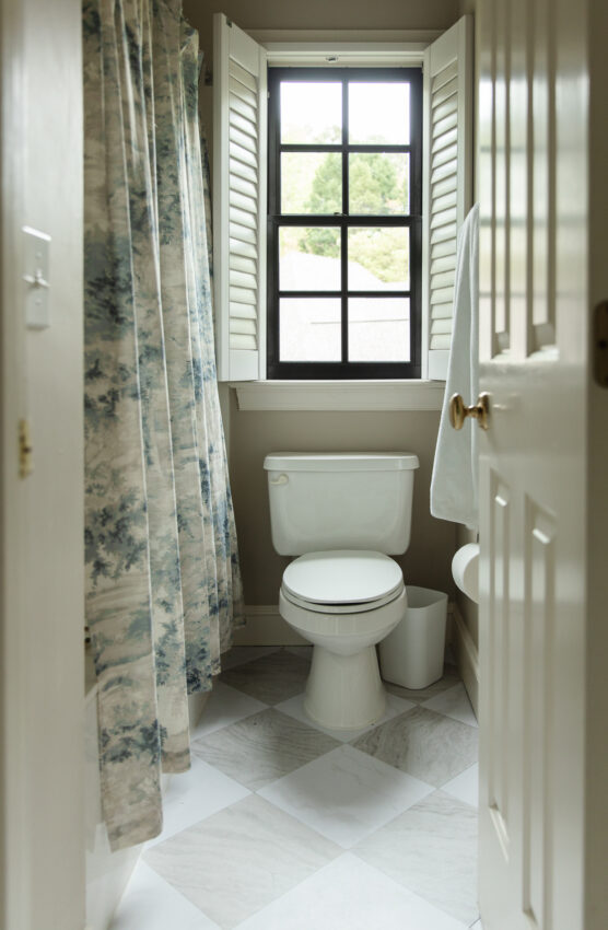 Small bathroom with a black-framed window, white toilet, and floral shower curtain, showcasing a simple and functional space.