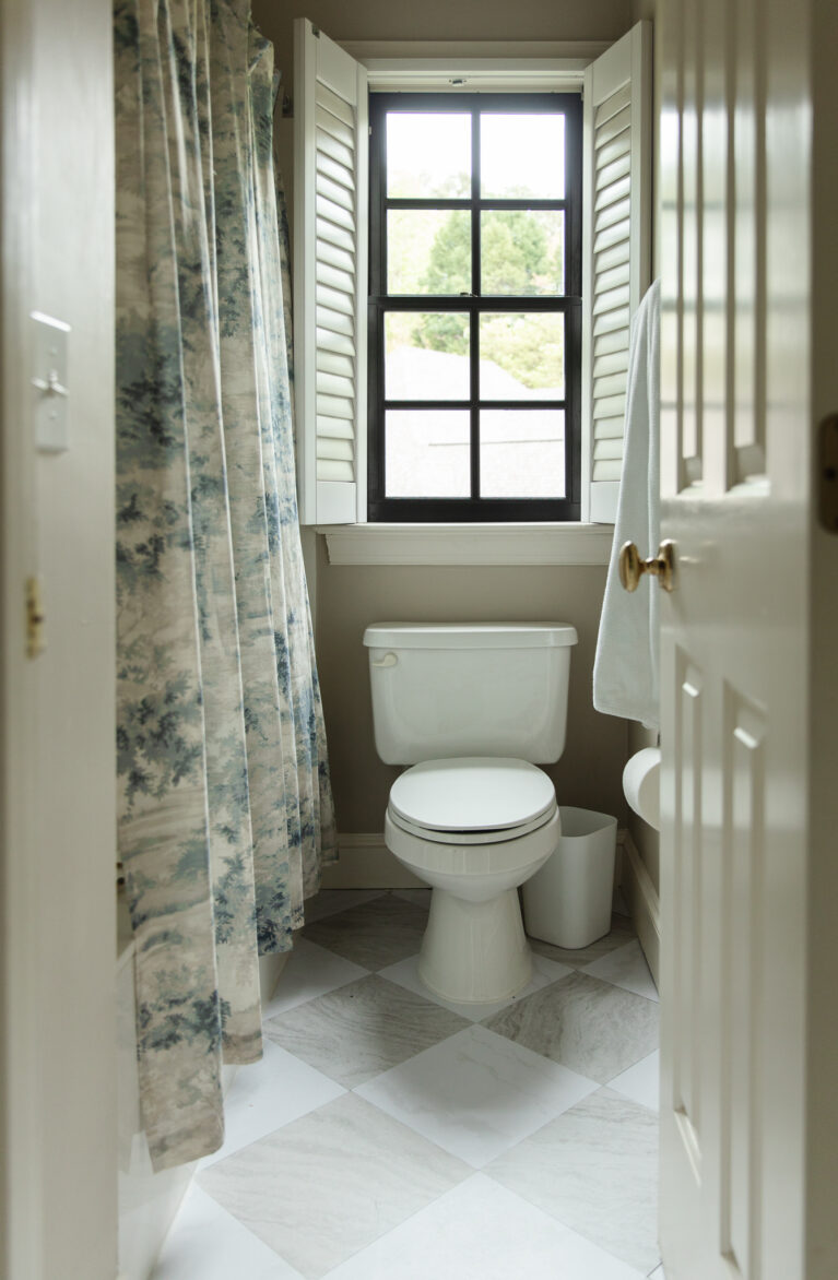 Small bathroom with a black-framed window, white toilet, and floral shower curtain, showcasing a simple and functional space.