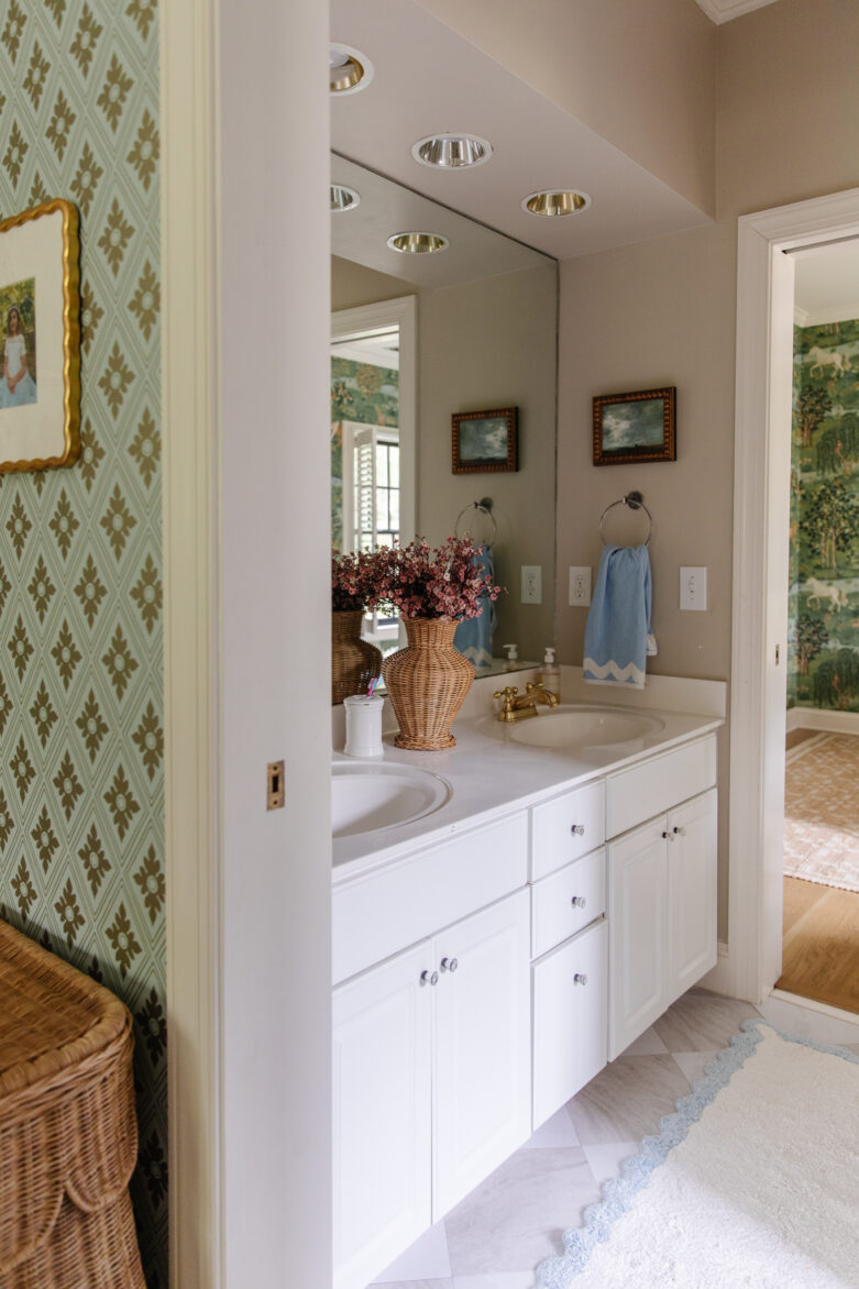Bright, airy Jack & Jill bathroom with white cabinetry, gold fixtures, and floral accents, showcasing a creative renovation idea inspired by a home improvement project.