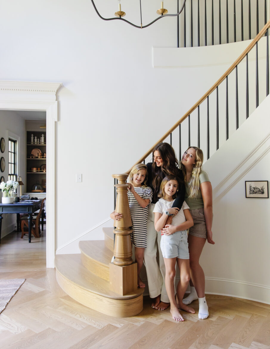Julia Marcum and her girls enjoying a moment together on a wooden staircase in a modern traditional entry.