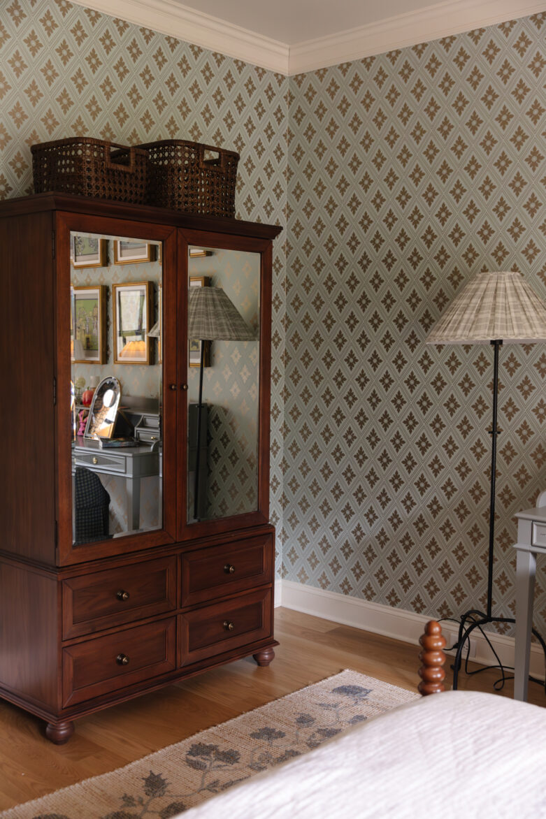 An inviting bedroom featuring a wooden wardrobe with mirrored doors, a tall floor lamp, and a patterned area rug, showcasing charming vintage decor and warm, natural lighting.