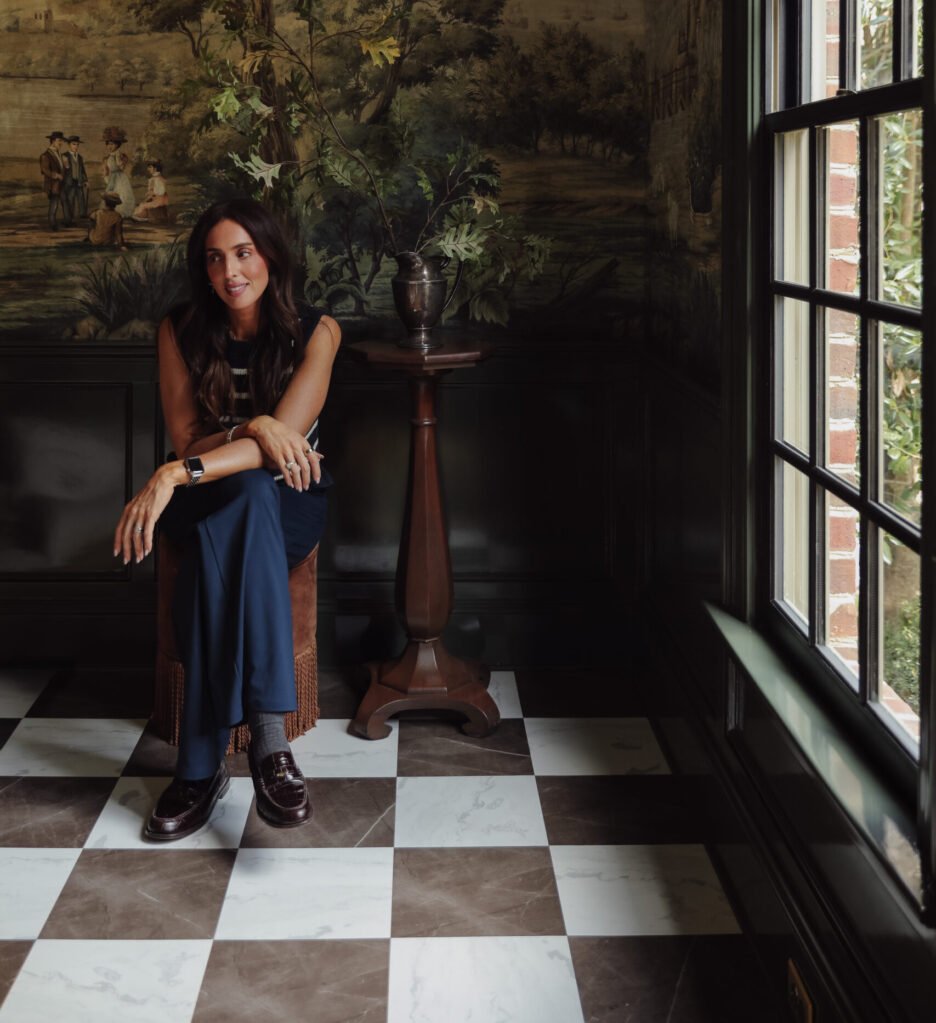 Bronze & white peel-and-stick floor tiles in a moody room that has a mural. Julia sits on an ottoman in the room.