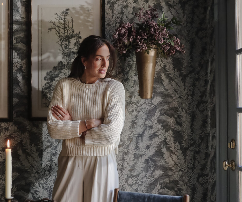 Julia Marcum standing in a beautifully decorated dining room with botanical wallpaper, framed artwork, and a vase of flowers, creating a warm and inviting atmosphere.