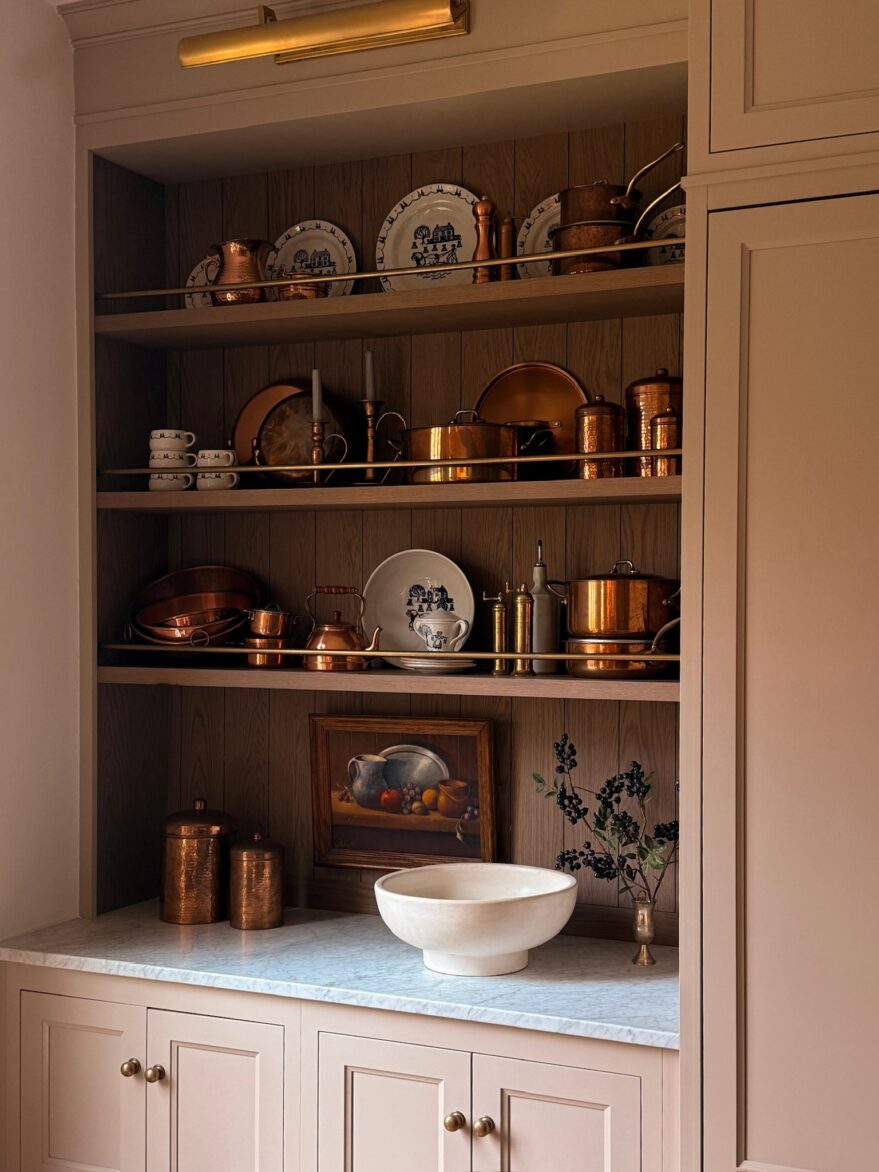 Elegant kitchen display featuring vintage copper pots, pans, and decorative plates arranged on open wooden shelves with a marble countertop.