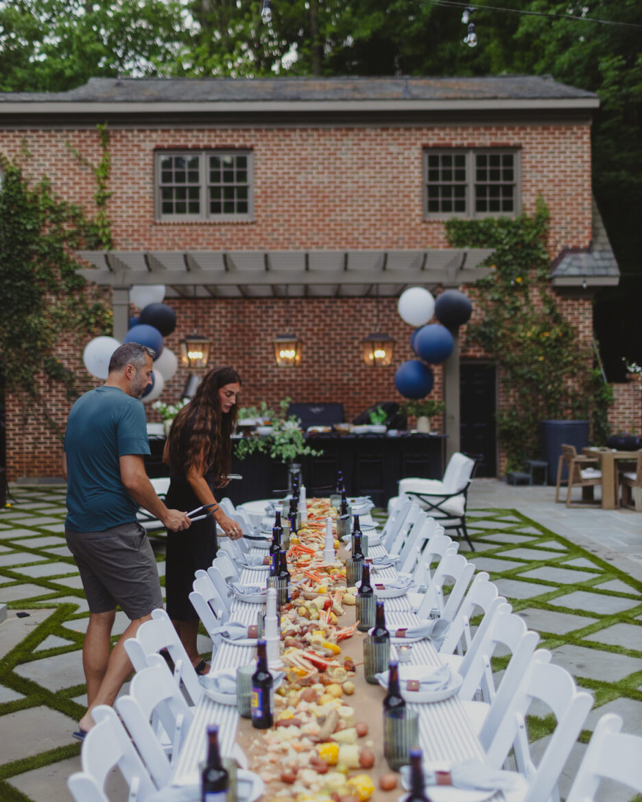 A beautifully arranged outdoor dinner table in a backyard, featuring drinks, food, and decorative elements for a summer gathering. Perfect for outdoor entertaining and family celebrations.