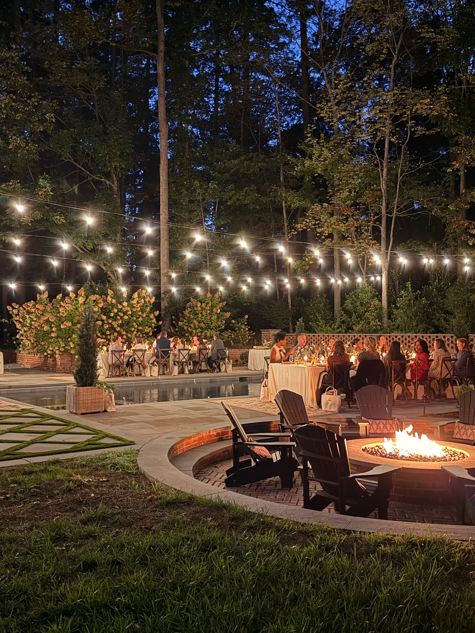 Outdoor backyard with string lights, fire pit, and seating area at night.