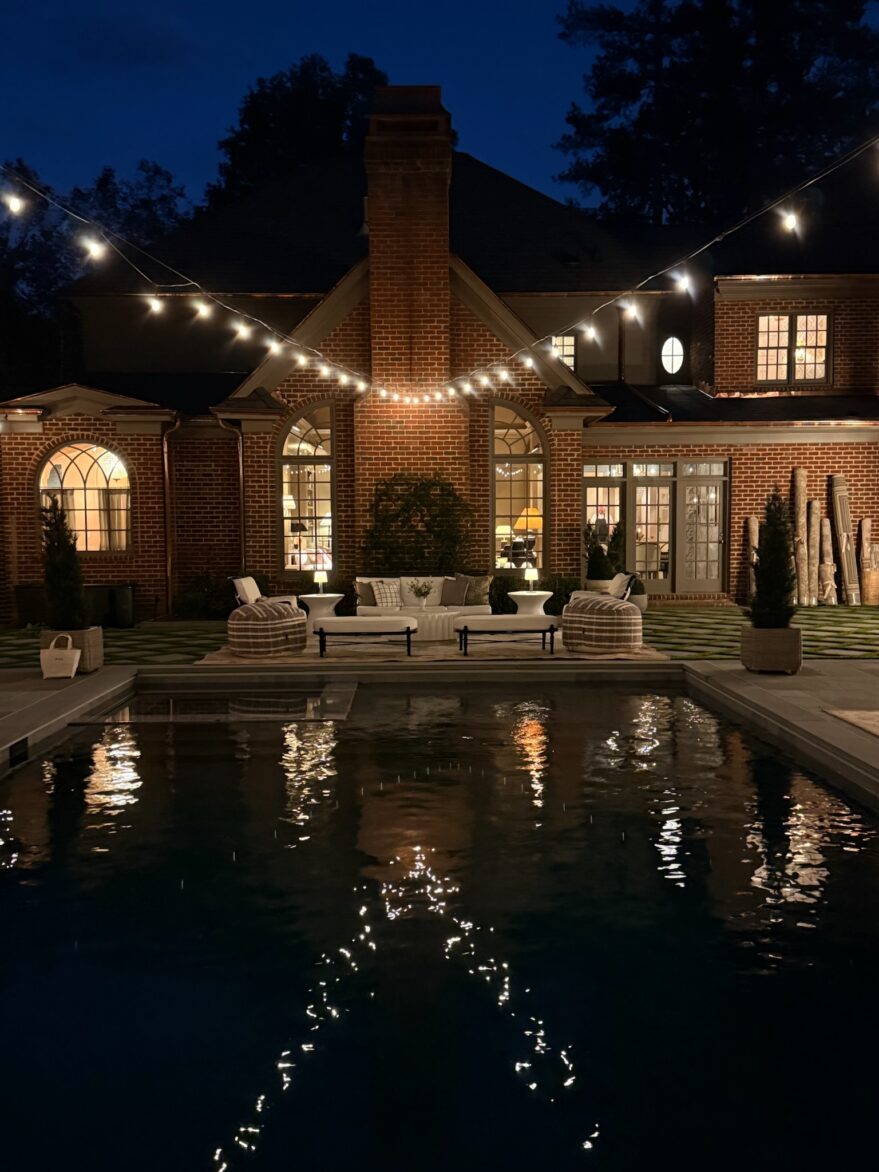 Beautiful nighttime view of a backyard patio with string lights, outdoor seating, and a swimming pool reflecting the lights, creating a cozy and inviting outdoor space.