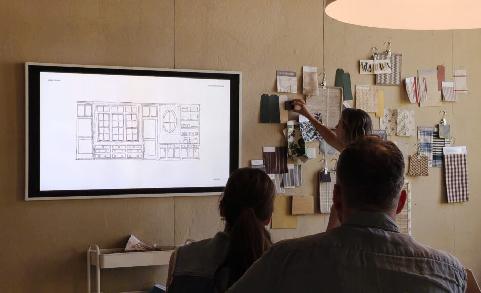 Interior design consultation with two clients reviewing a home layout on a large screen in a creative studio.