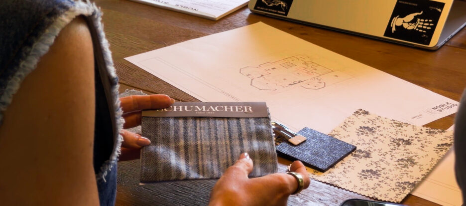 A person holding fabric swatches and working on interior design sketches at a wooden desk, showcasing fabric samples, color palettes, and design plans for home renovation projects.