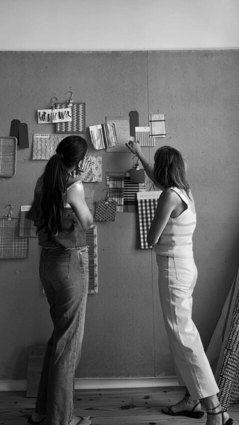 Women collaborating on interior design project, hanging fabric swatches on a wall for home decor inspiration.