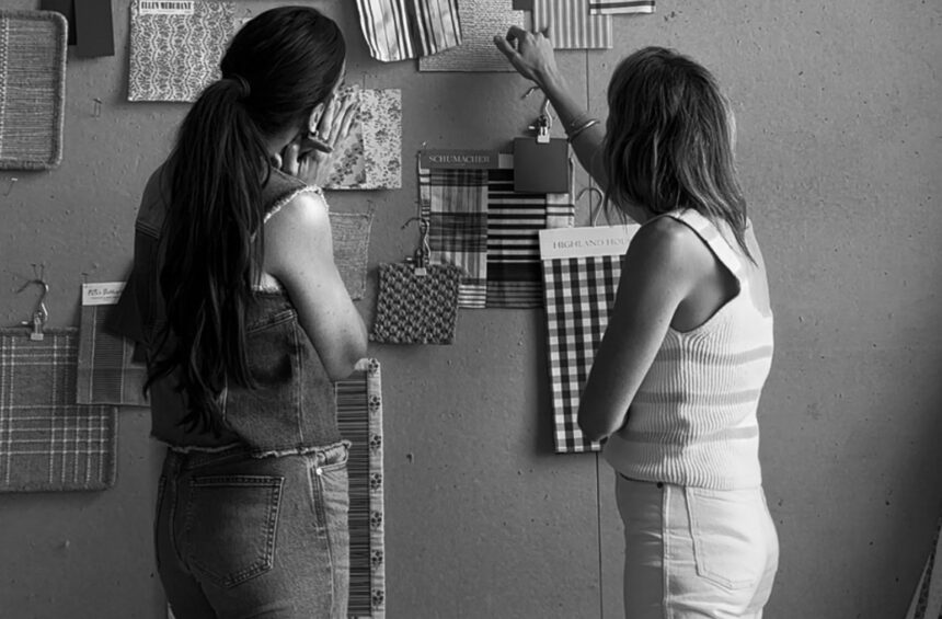 Women collaborating on interior design project, hanging fabric swatches on a wall for home decor inspiration.