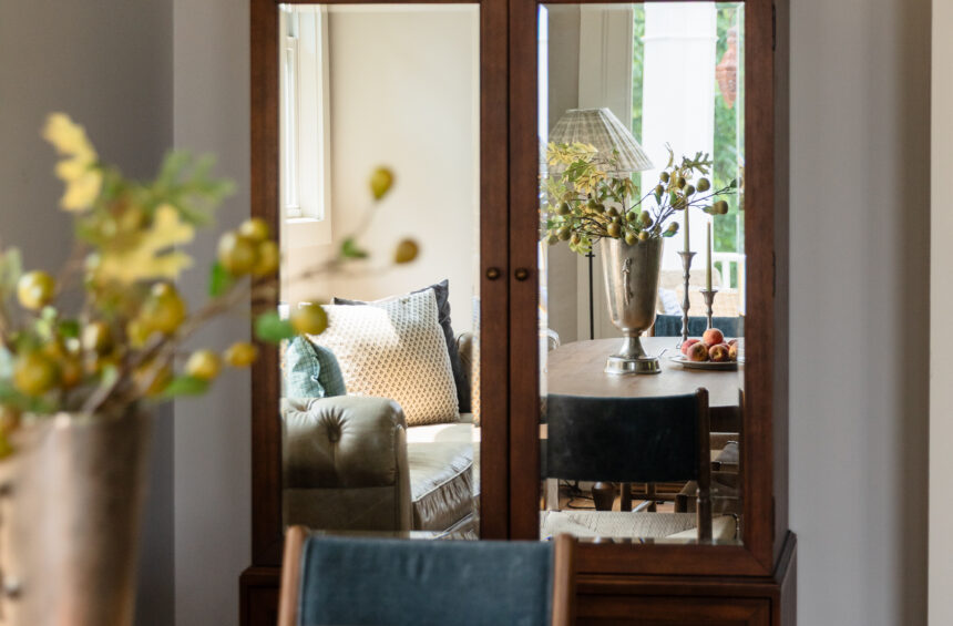 Modern traditional dining room styling showcasing a rich wood armoire with mirrors reflecting the room, styled with vintage-inspired tabletop decor, a textured black vase, and a gold-framed landscape painting.